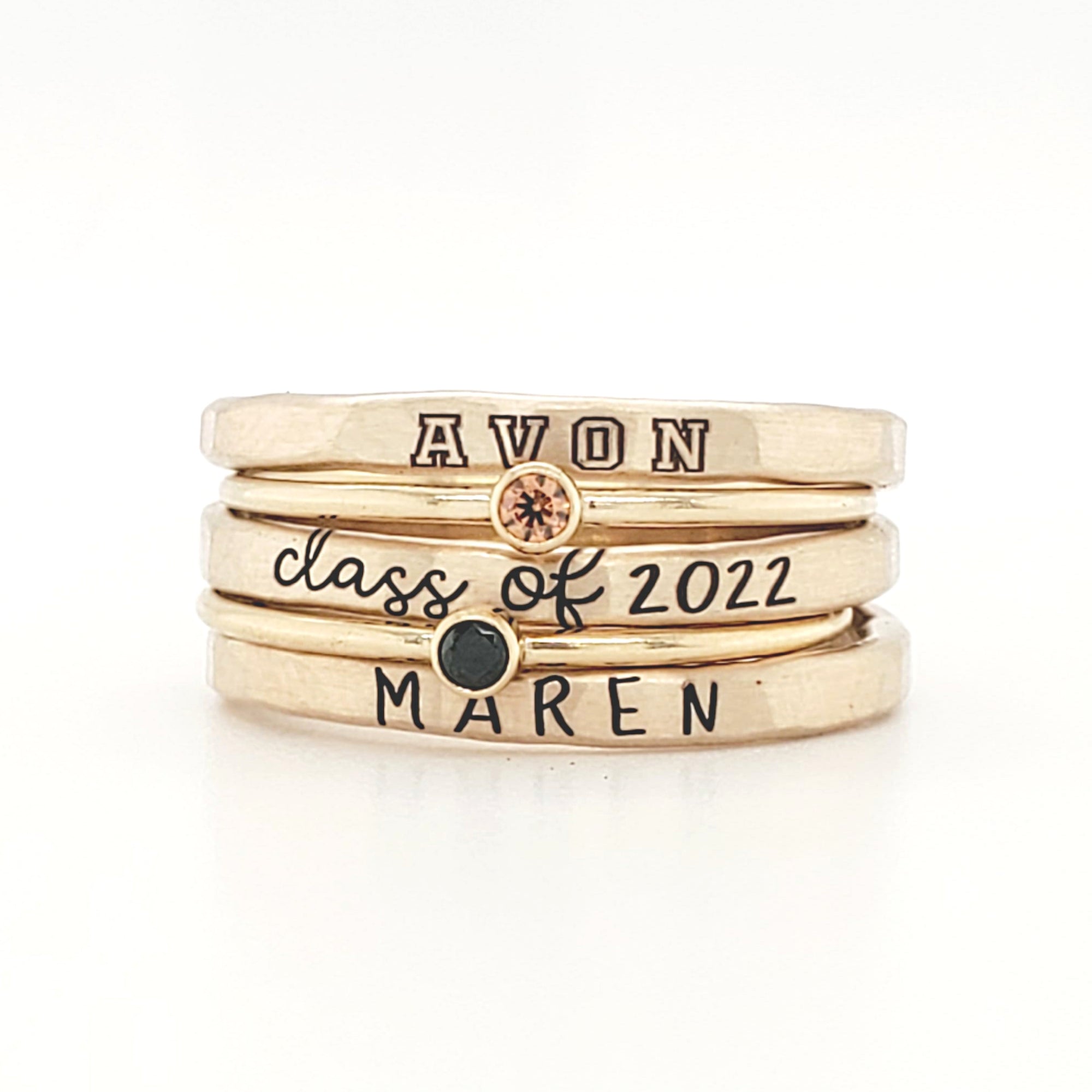 A set of three stackable rings made of yellow gold, with two gemstones, and personalized engravings including 'AVON', 'class of 2022', and 'MAREN'.