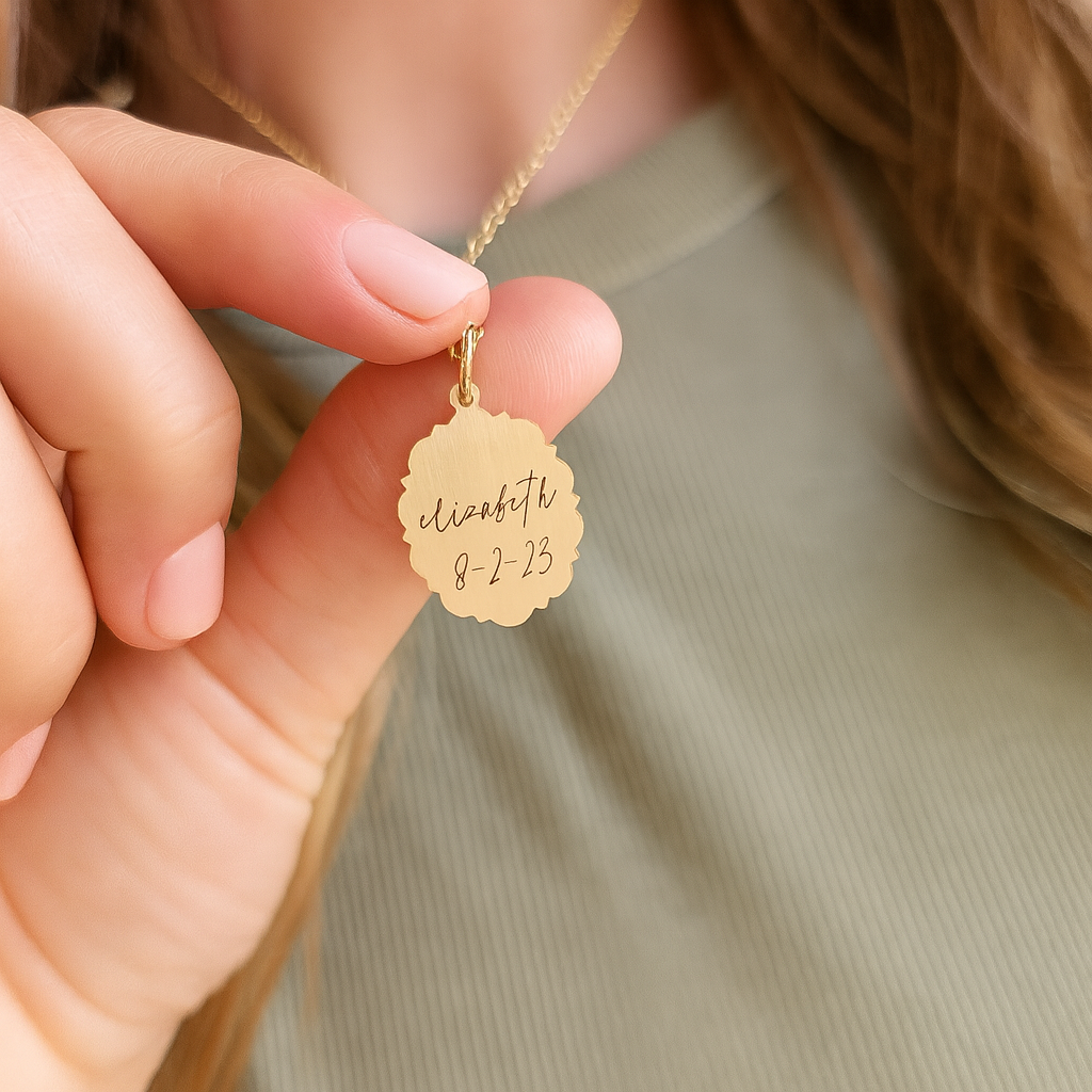 Gold necklace with a engraved pendant held by a hand against a neutral background