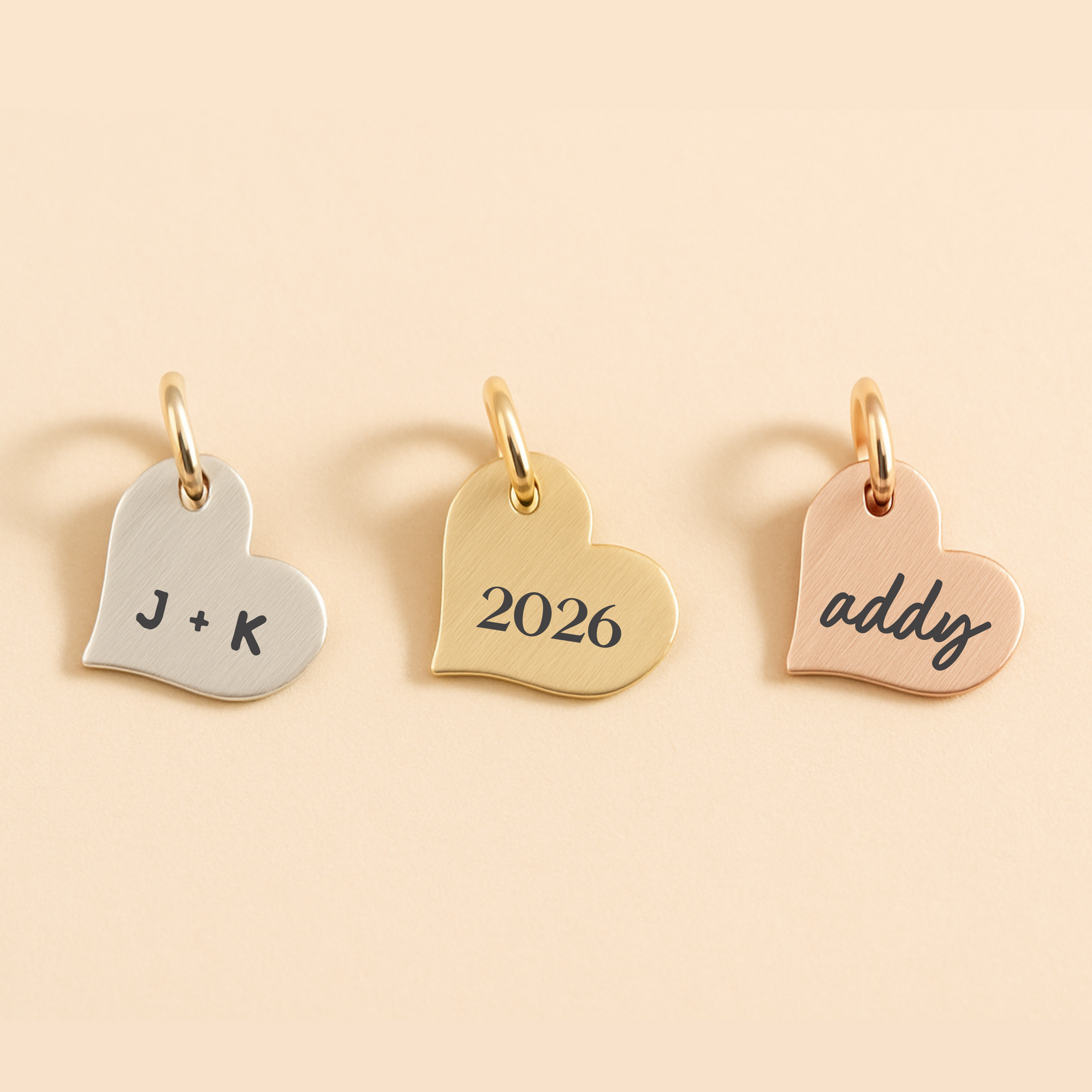 Three heart-shaped gold pendants with engraved text on a beige background
