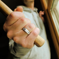 Hand wearing a silver ring with engraved numbers, holding a wooden handle.