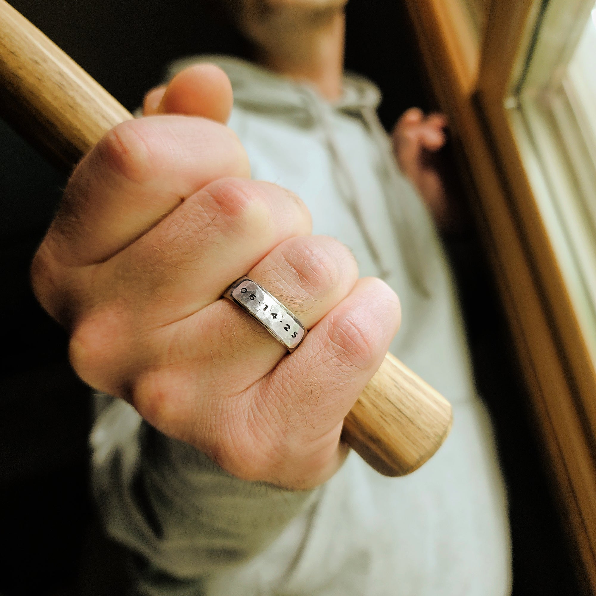 Hand wearing a silver ring with engraved numbers, holding a wooden handle.