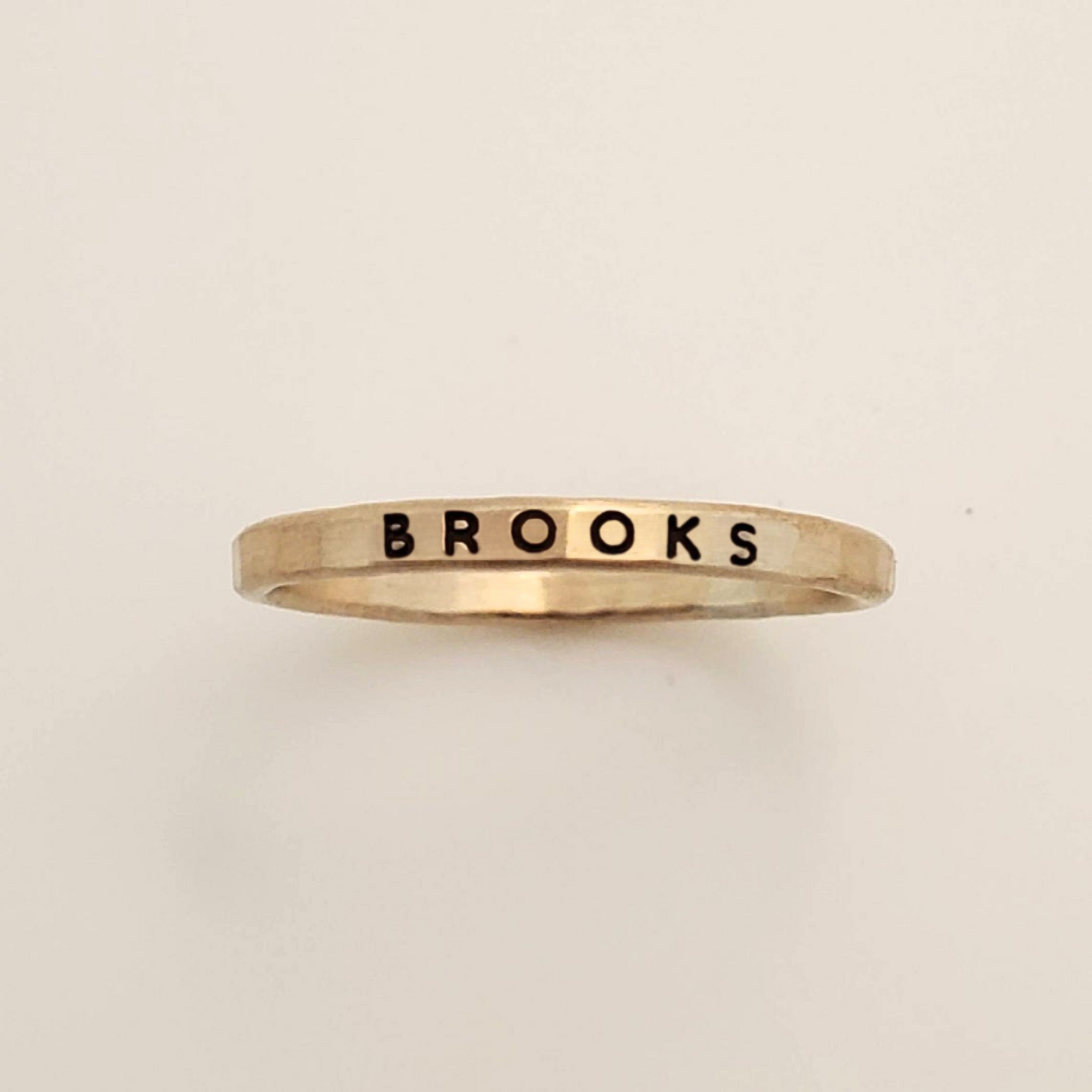 Gold ring with 'BROOKS' engraving on a beige background