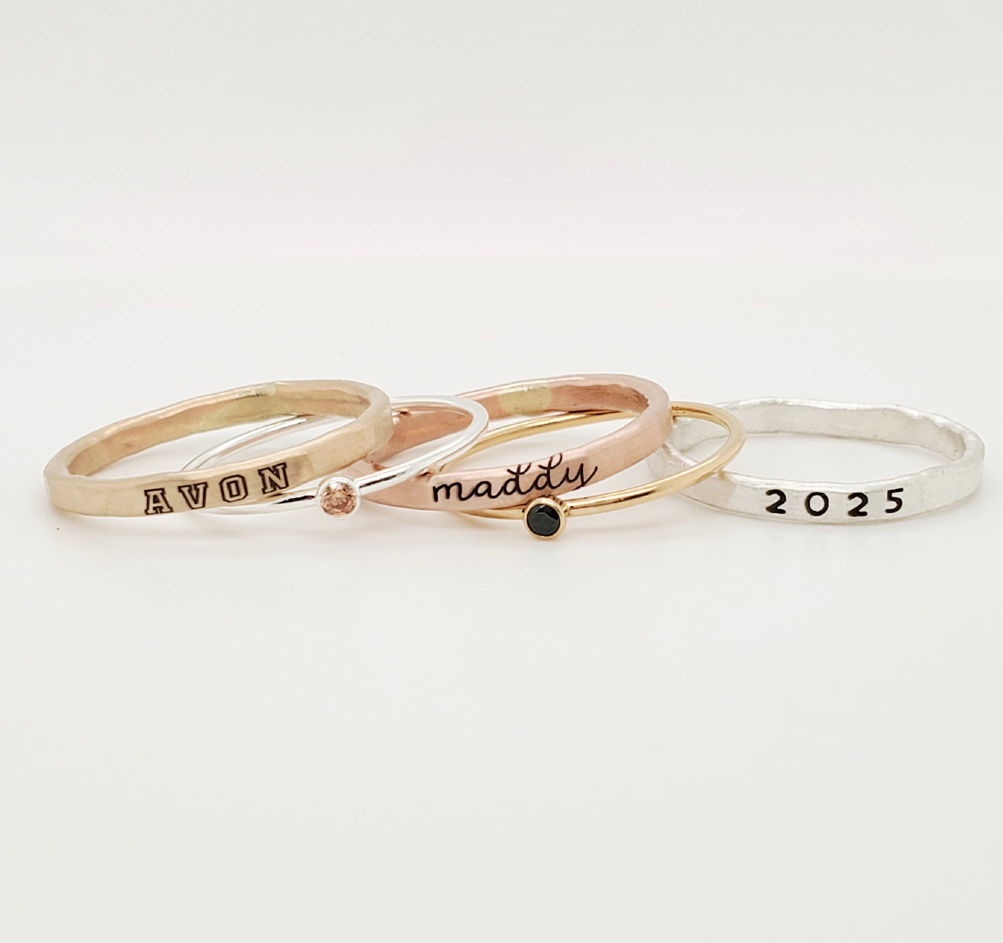 A set of three stackable rings made of yellow gold and sterling silver with two gemstones, and personalized engravings including 'AVON', 'class of 2025', and 'MADDY'.