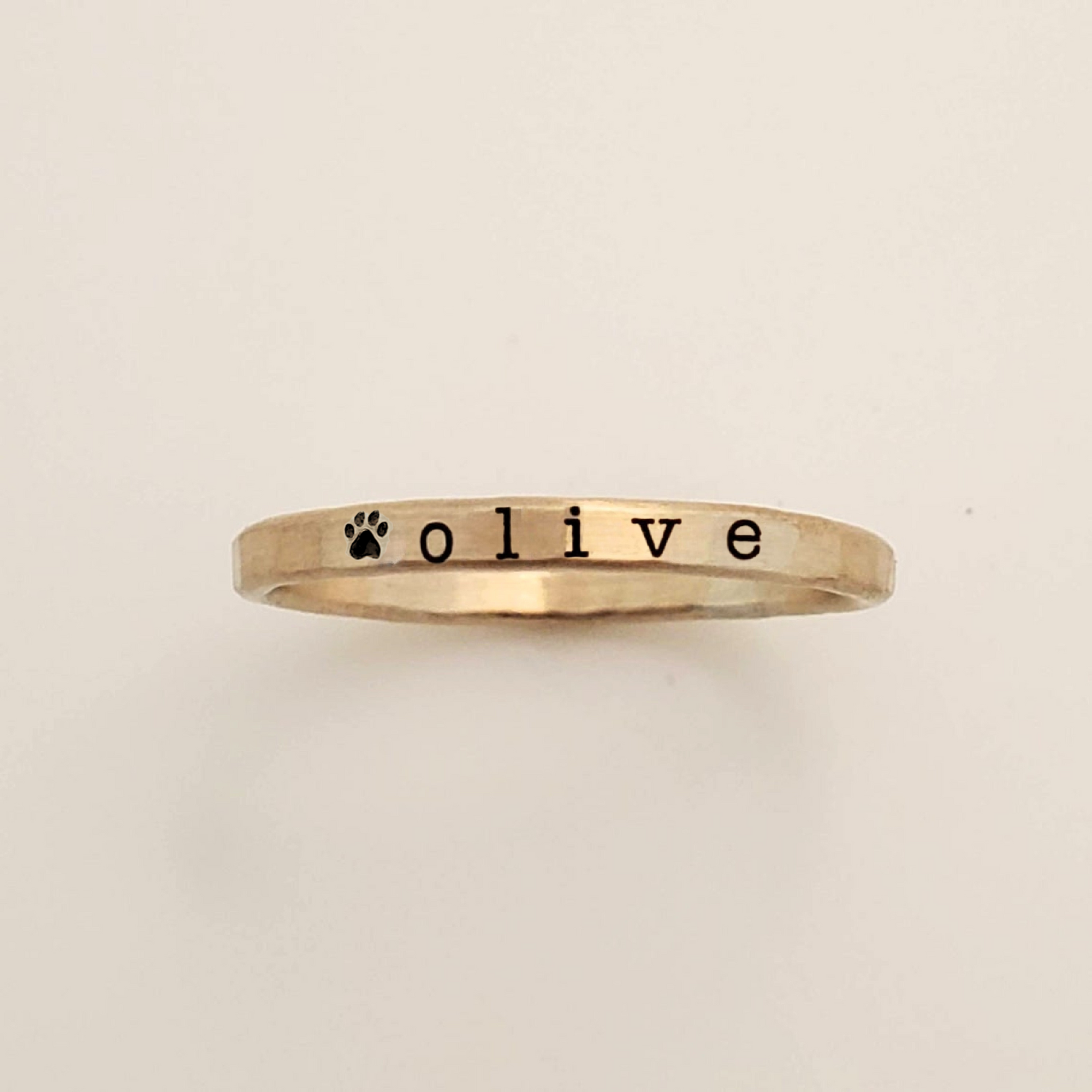 Gold ring with 'olive' and a paw print on a beige background