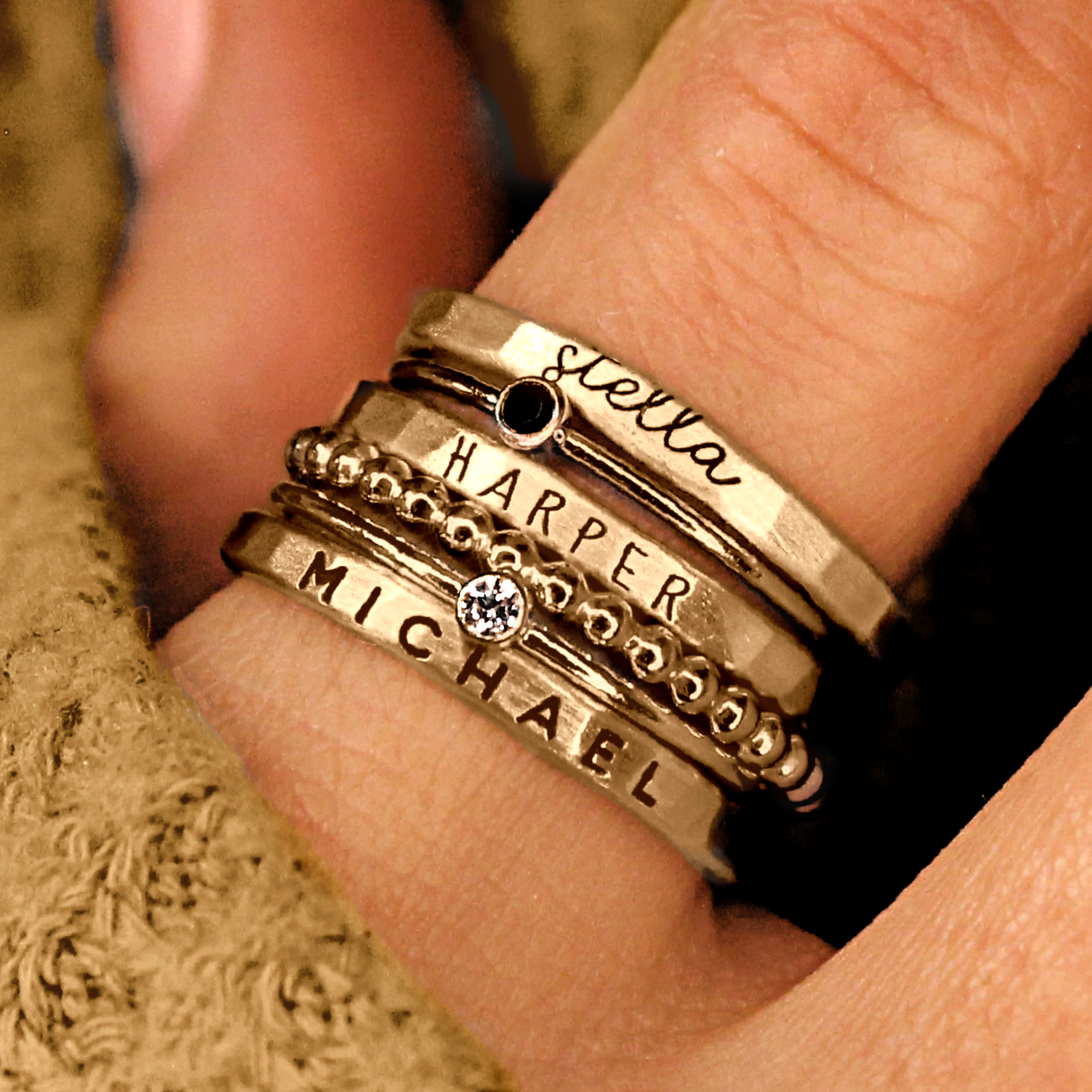 A set of gold stacking name rings with personalized engravings on each ring, displayed on a person's hand.