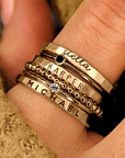 A set of gold stacking name rings with personalized engravings on each ring, displayed on a person's hand.