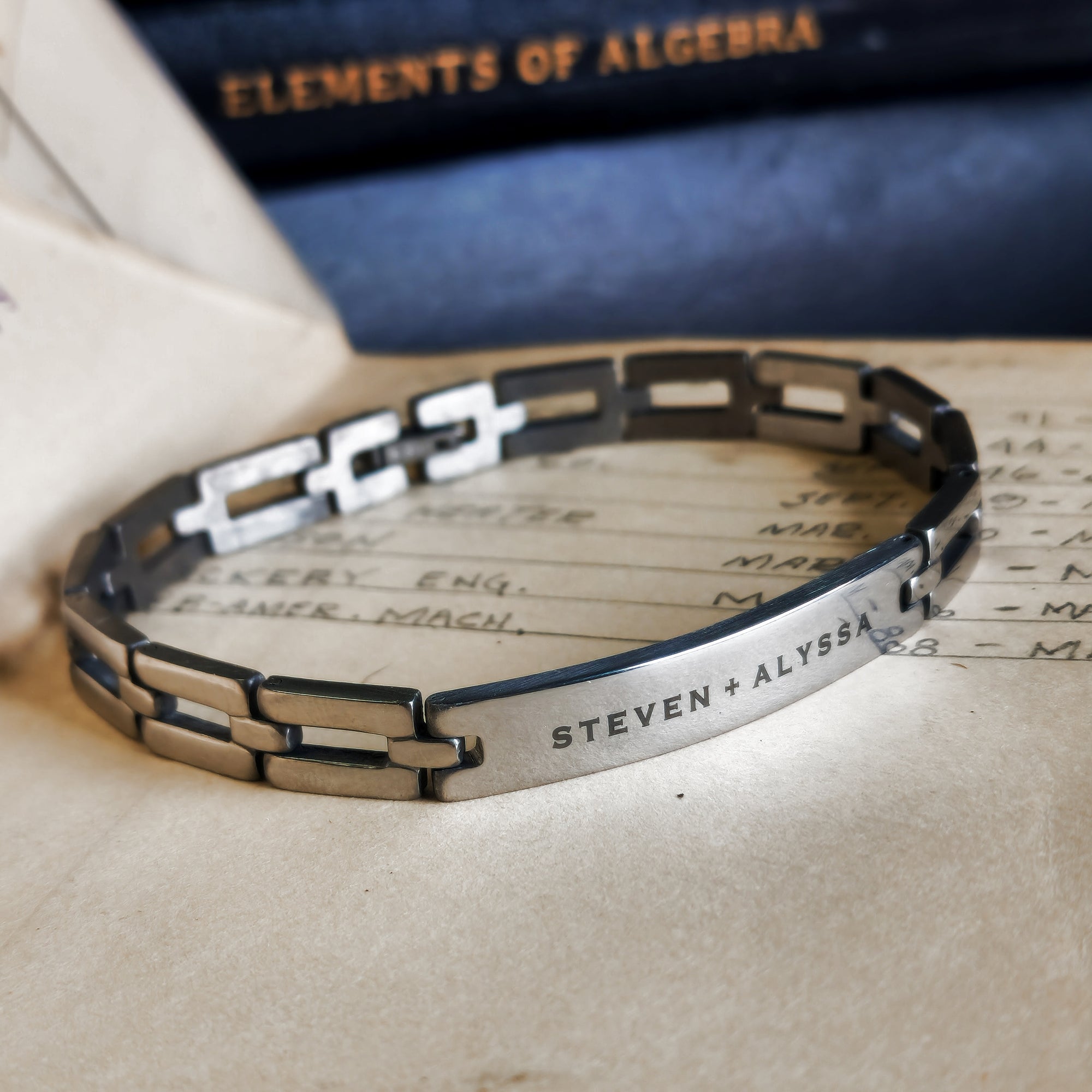 Silver bracelet with engraved names on a surface with an old book in the background