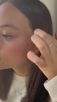 Woman placing gold U-shaped earrings on ear in video demo