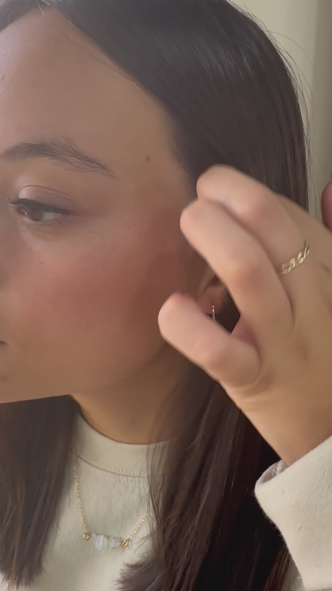 Woman placing gold U-shaped earrings on ear in video demo