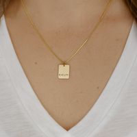 Gold necklace with a tag worn by a person on a white background