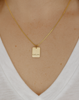 Gold necklace with a tag worn by a person on a white background