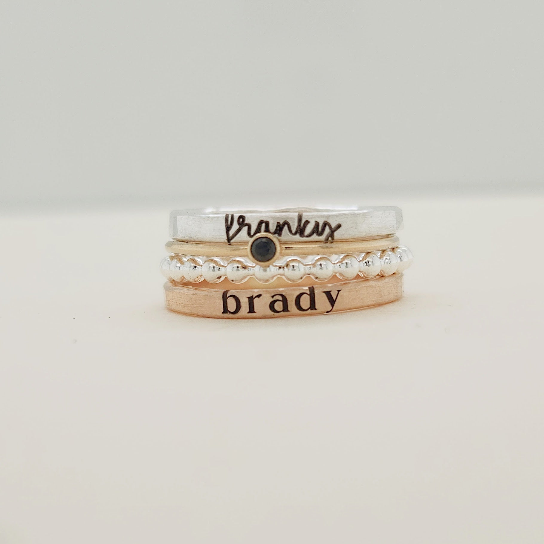 A set of four stackable rings, with the top ring displaying the word 'brady' and a small heart pattern, and a band ring with 'brady' written on it.