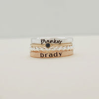 A set of four stackable rings, with the top ring displaying the word 'brady' and a small heart pattern, and a band ring with 'brady' written on it.
