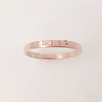 A rose gold-colored stacking name ring with the name 'nico' hand-stamped on it.