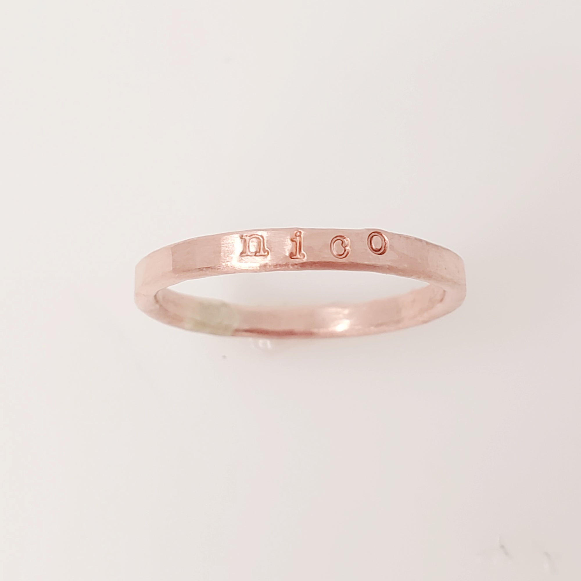A rose gold-colored stacking name ring with the name 'nico' hand-stamped on it.