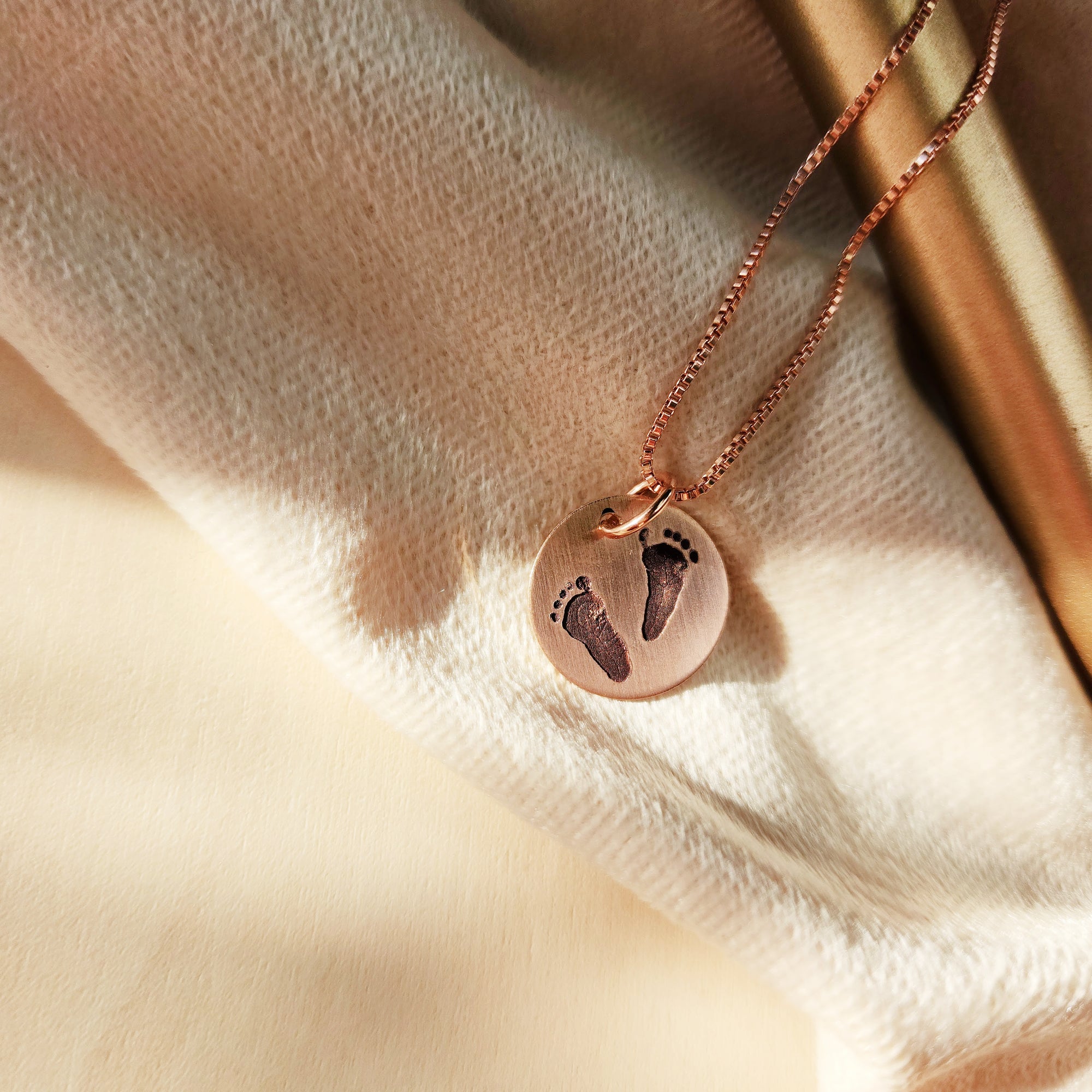 Rose gold necklace with footprints on a soft fabric background