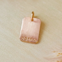 Rose gold pendant with 'CORBEN' engraving on a beige background
