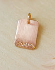 Rose gold pendant with 'CORBEN' engraving on a beige background