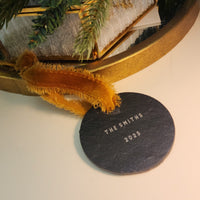 Decorative slate disc with 'The Smiths 2025' text, placed on a surface with a gold frame and greenery.