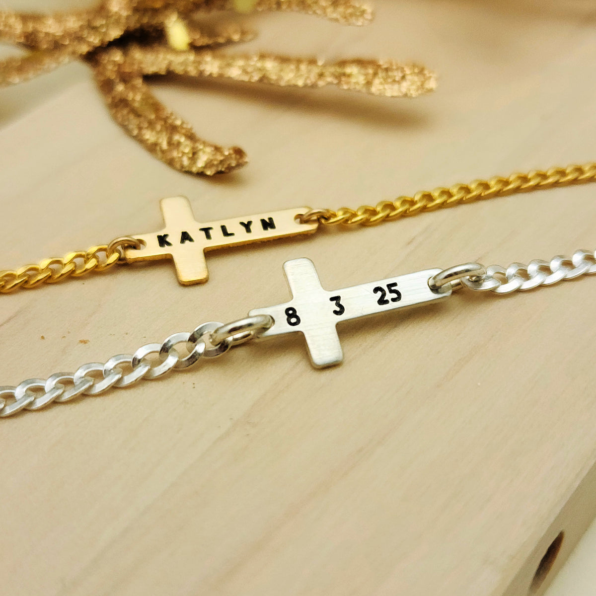 Two gold and silver bar bracelets with engraved names and numbers on a beige background.
