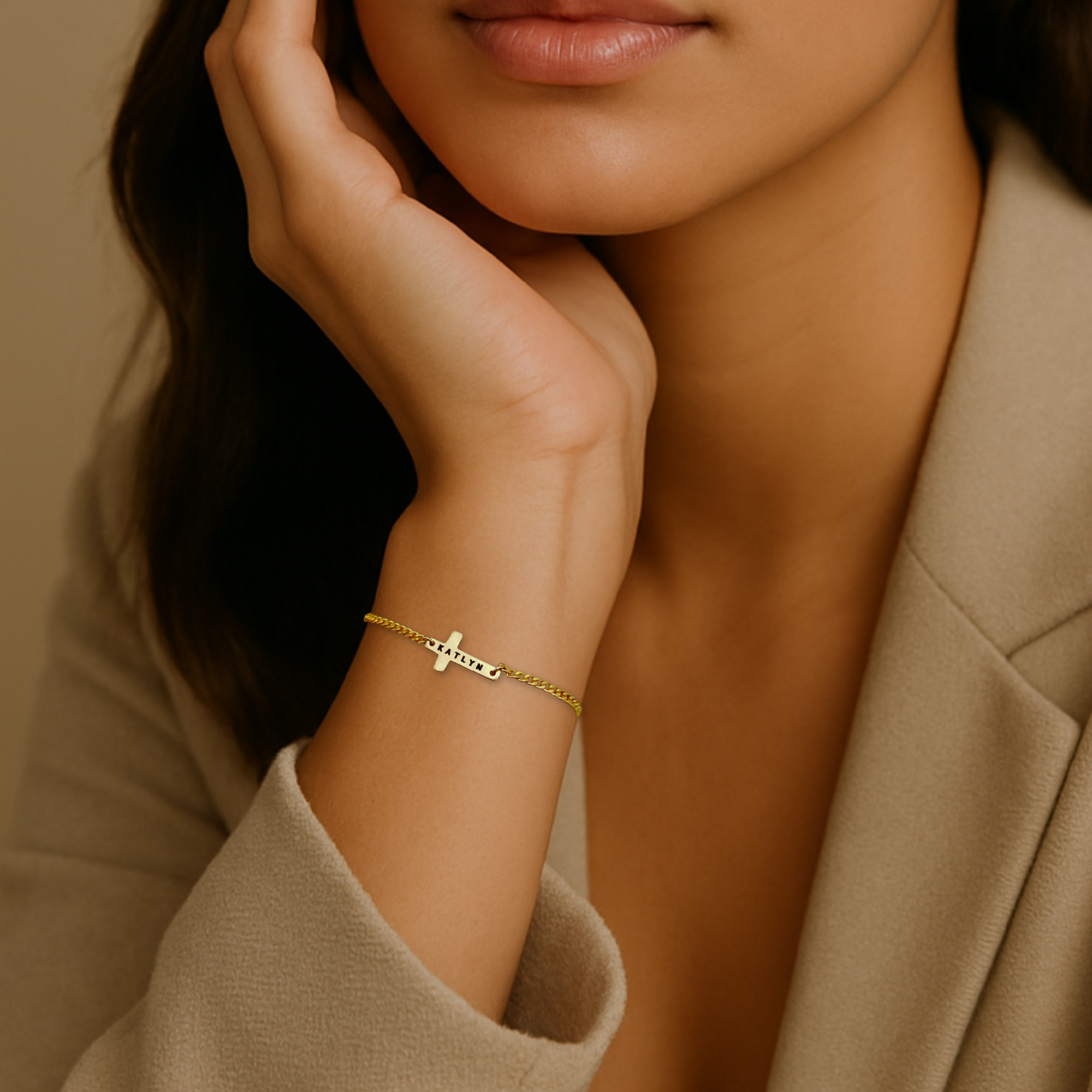 Close-up of a woman's hand wearing a gold bracelet with a cross charm, against a neutral background.