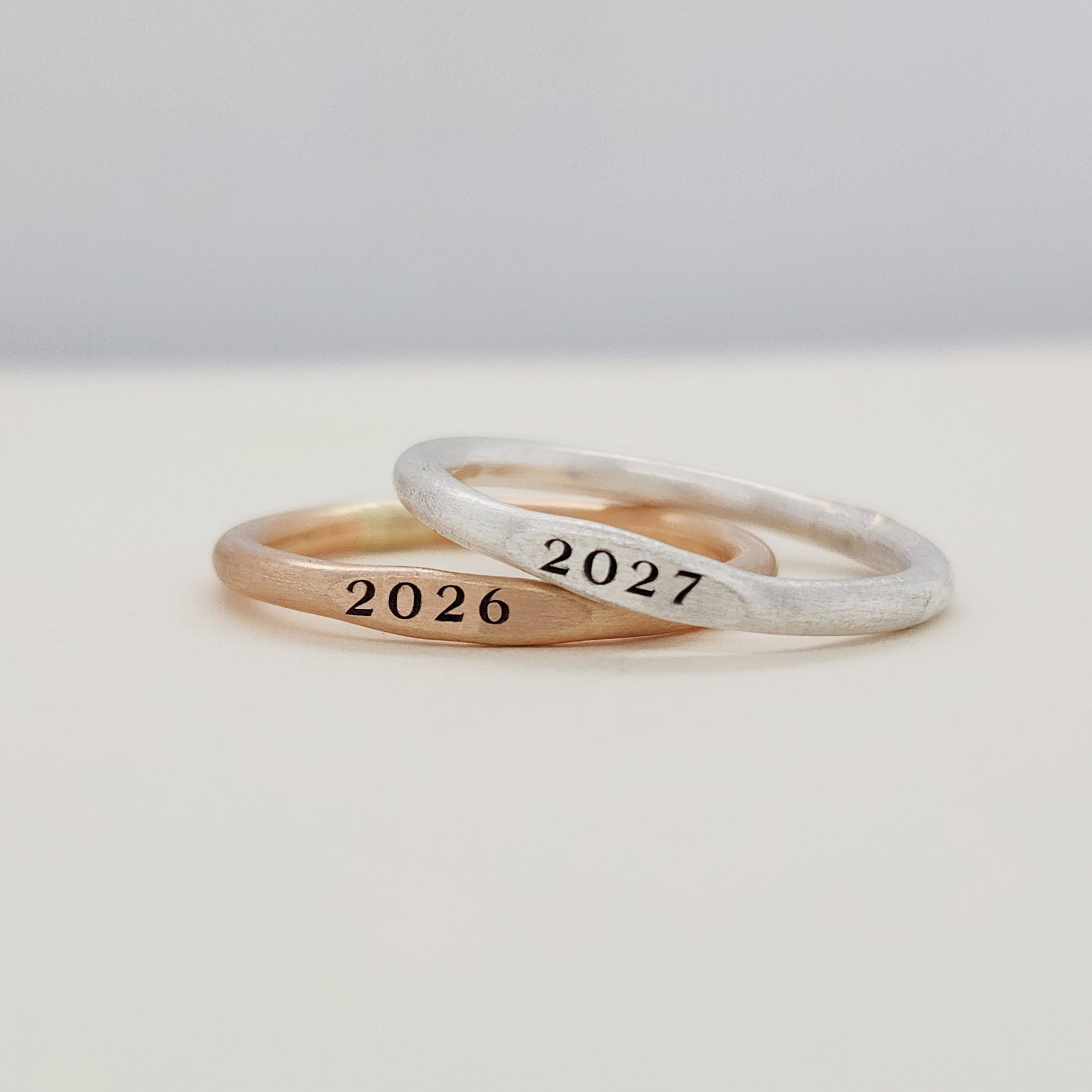 Two signet year stacking rings, one with '2026' and the other with '2027', displayed on a white surface.