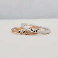 Two signet year stacking rings, one with '2026' and the other with '2027', displayed on a white surface.