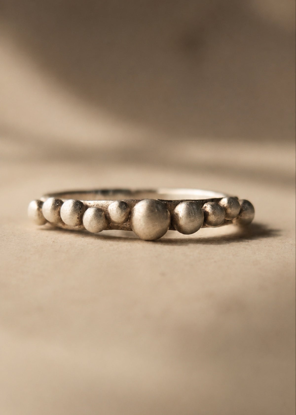 Silver ring with bead-like design on a beige background