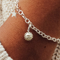 A woman's wrist wearing a silver charm bracelet with a star-shaped charm and a small sun charm attached to it.