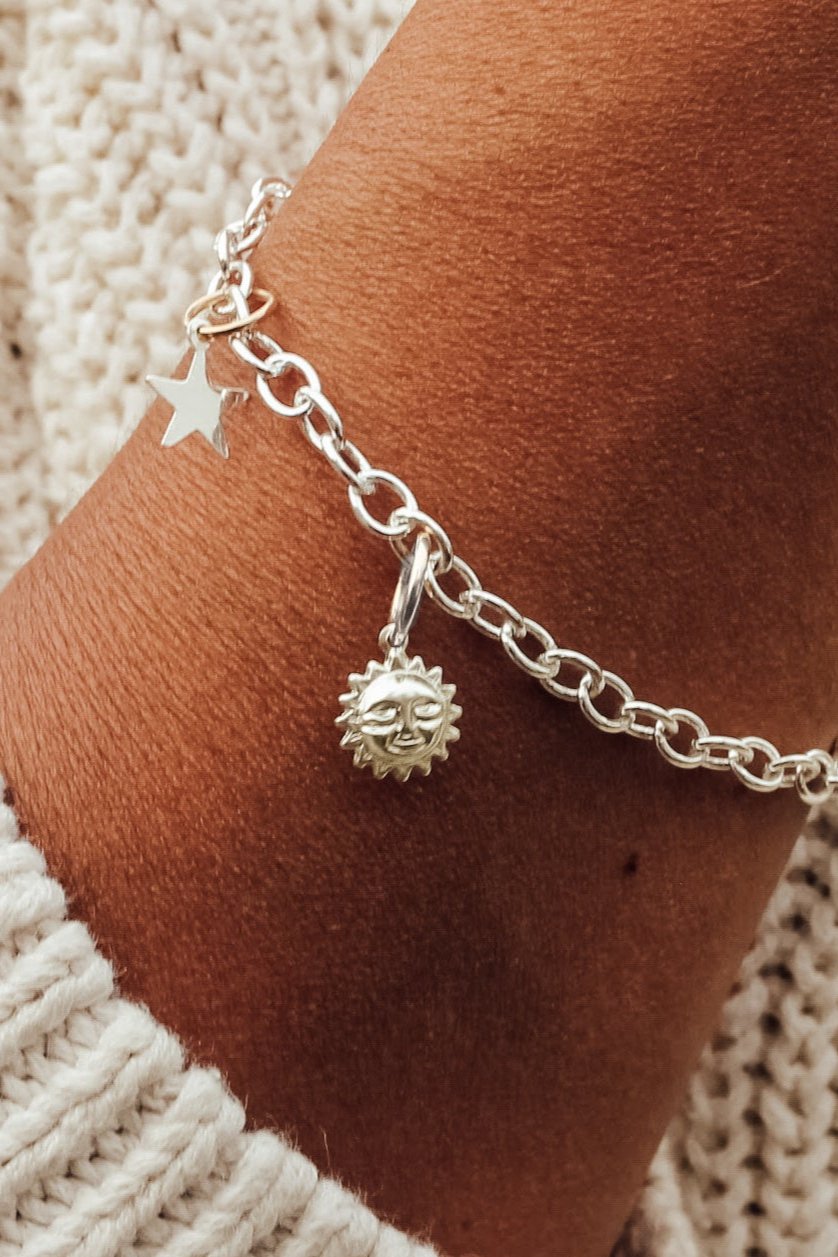 A woman's wrist wearing a silver charm bracelet with a star-shaped charm and a small sun charm attached to it.