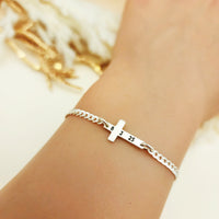 Silver bracelet with a cross charm on a wrist against a neutral background