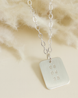 Silver date-stamped pendant necklace displayed on pampas grass background