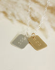 Silver and gold date-stamped pendant necklaces layered together on a silver chain, displayed on a cream background.