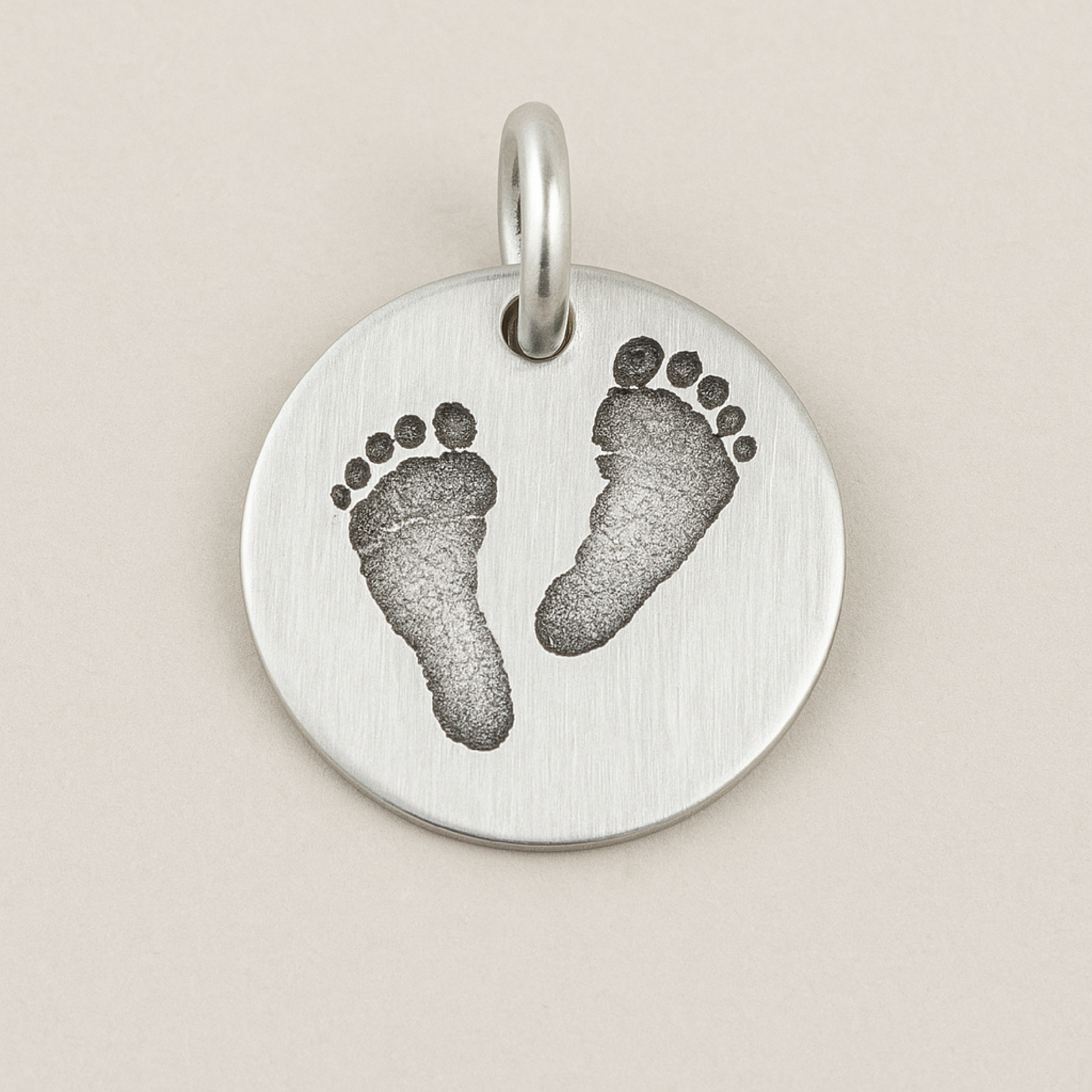 Silver pendant with footprints on a beige background