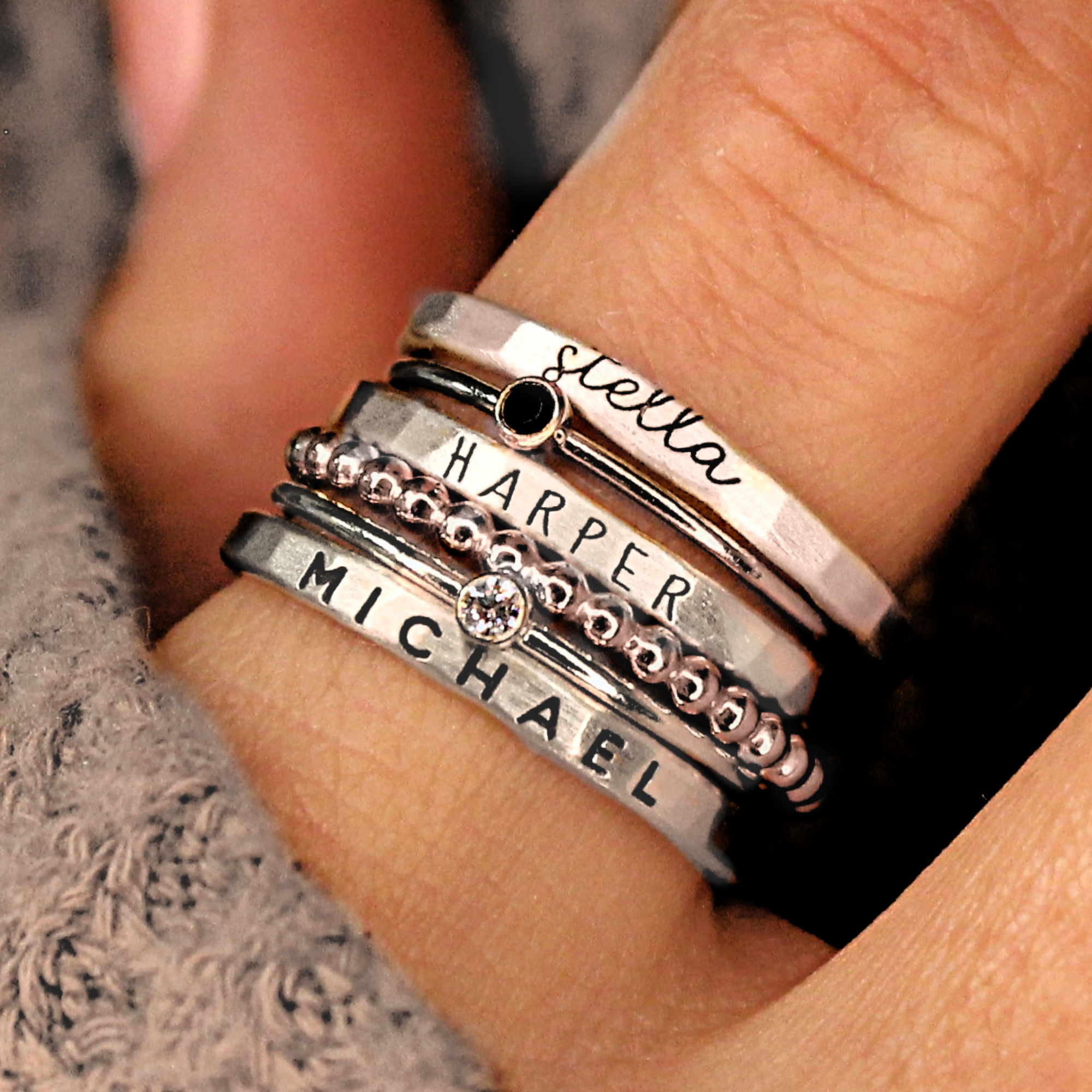 A set of silver stacking name rings with personalized engravings on each ring, displayed on a person's hand.