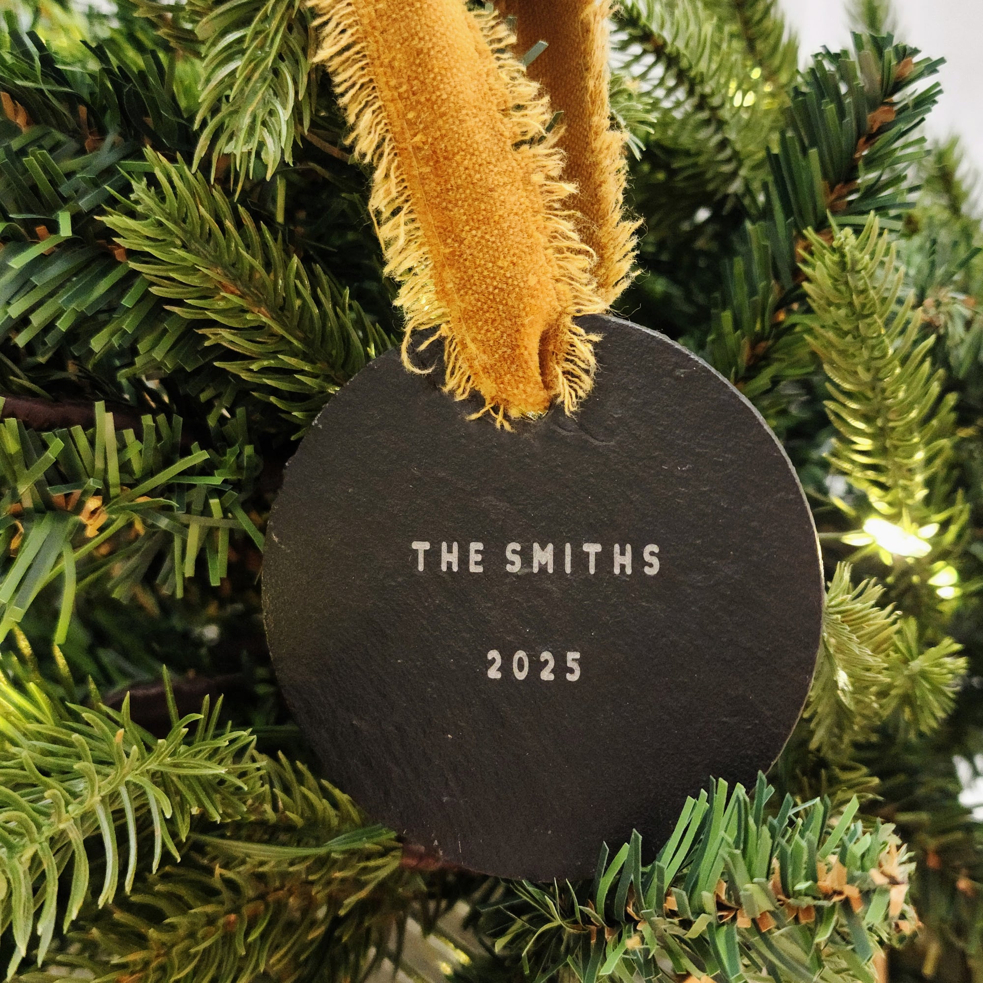 Round black ornament with 'The Smiths' and '2025' text, hanging on a Christmas tree.