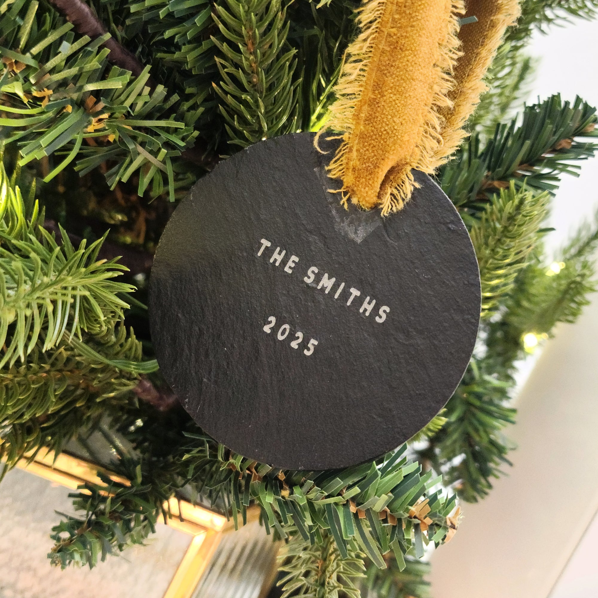 Round slate ornament with 'The Smiths 2025' text on a Christmas tree.
