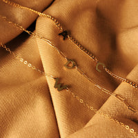 Gold necklaces with letter pendants on a beige fabric background