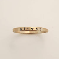 A gold-colored ring with the name 'oliver' engraved in a typewriter-style font.