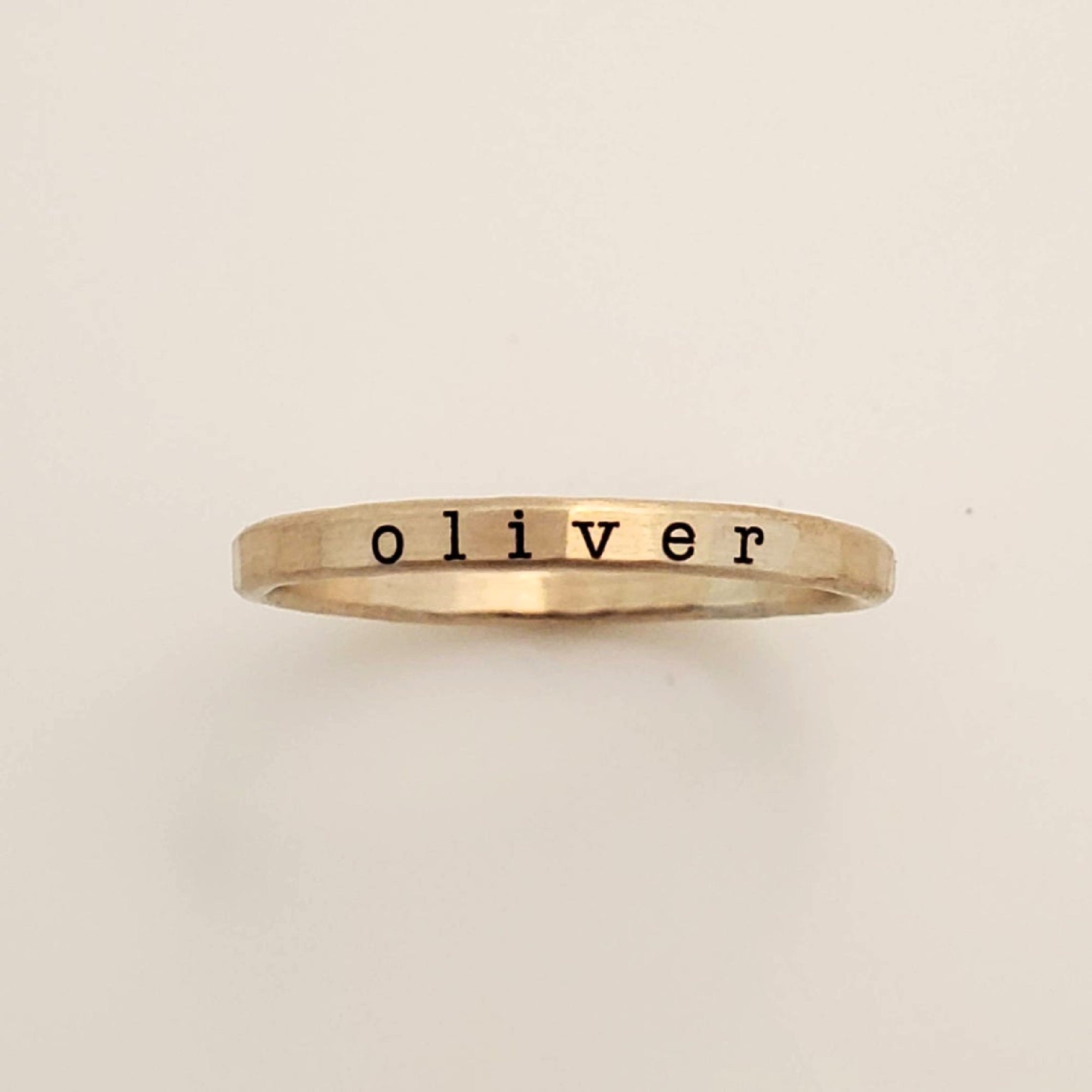 A gold-colored ring with the name 'oliver' engraved in a typewriter-style font.