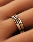 Two gold rings with engraved text on a finger