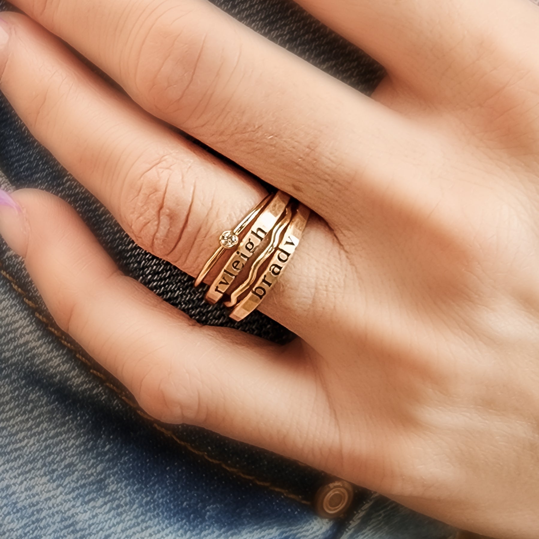 A person's hand showcasing a stack of gold-filled rings, with the focus on the rings' texture and shine.
