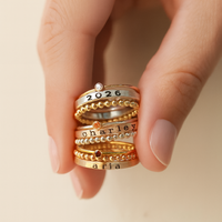 Stack of gold and silver rings with engraved names on a beige background