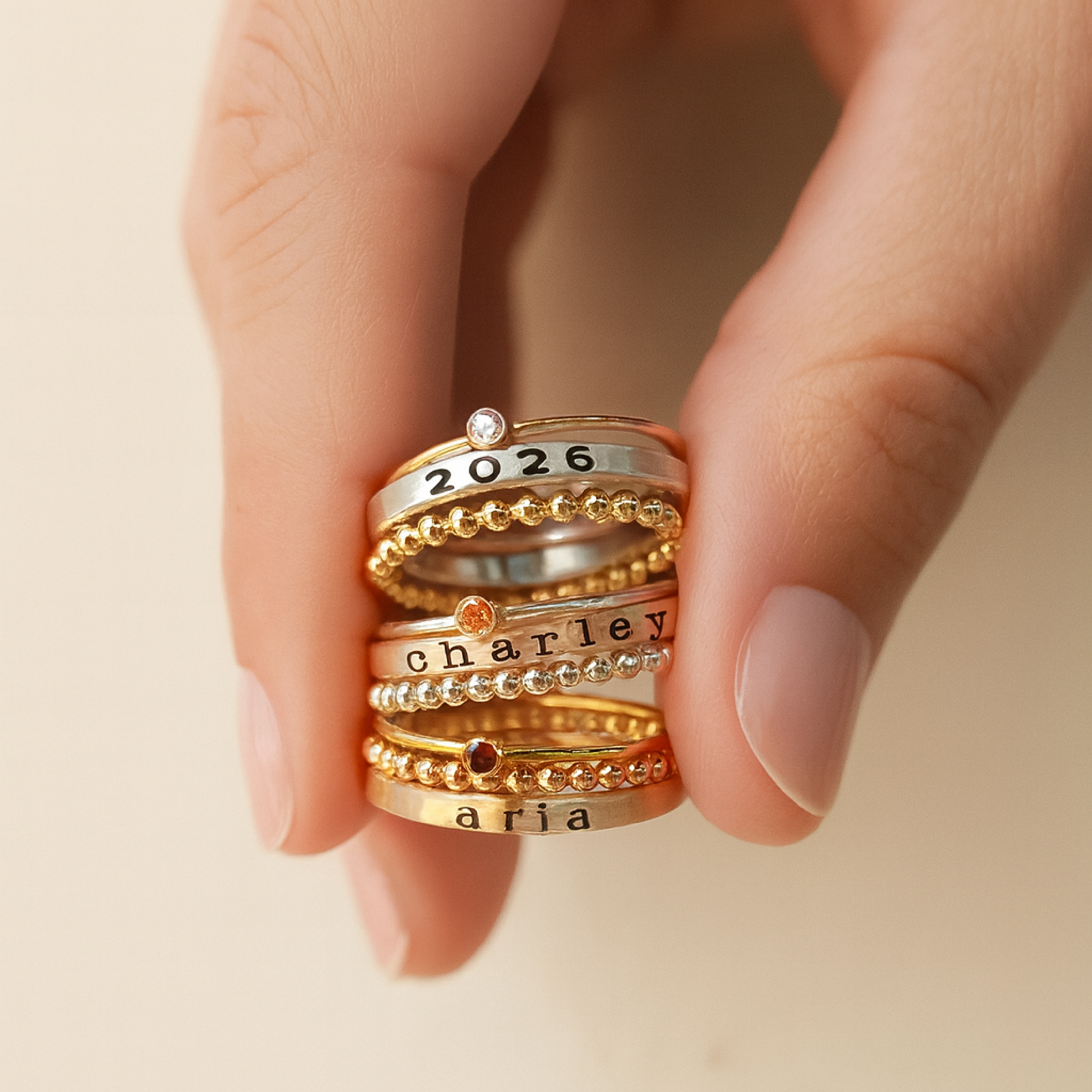 Stack of gold and silver rings with engraved names on a beige background