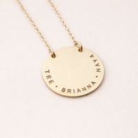 Gold necklace with engraved names on a light pink background