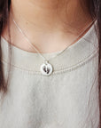 A person wearing a grey sweater and a necklace with an engraved footprint pendant on a silver chain.