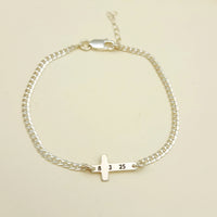 Gold bracelet with a small cross charm on a beige background