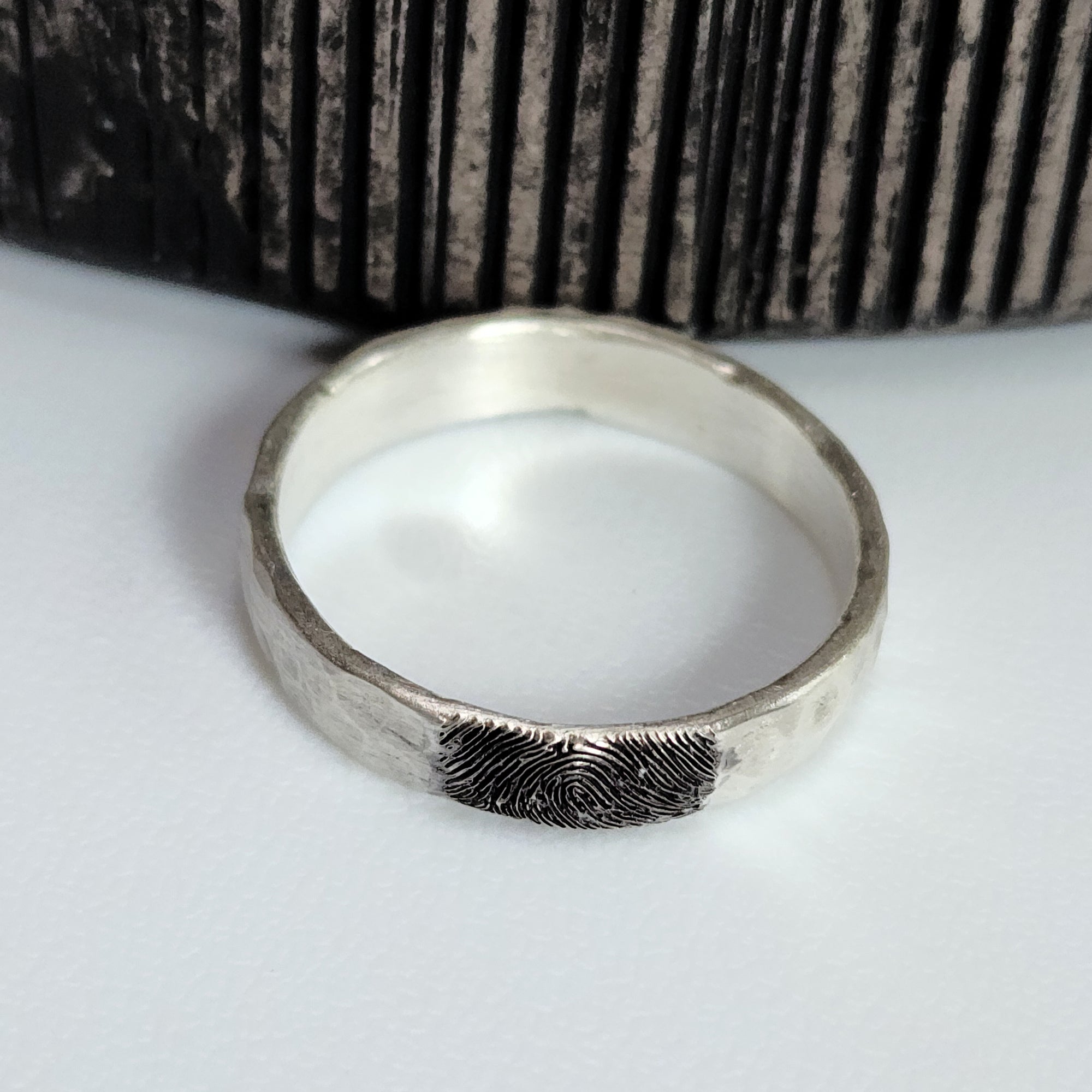 Silver ring with fingerprint design on a white surface