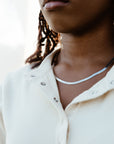 A close-up image of a person wearing a sterling silver herringbone chain necklace with a lobster claw clasp.
