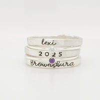A set of three stackable rings made of yellow gold, with two gemstones, and personalized engravings including 'BROWNSBURG', 'class of 2025' and 'MAREN'.